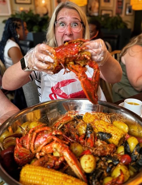 A happy Claw Club guest holding a lobster above a seafood feast